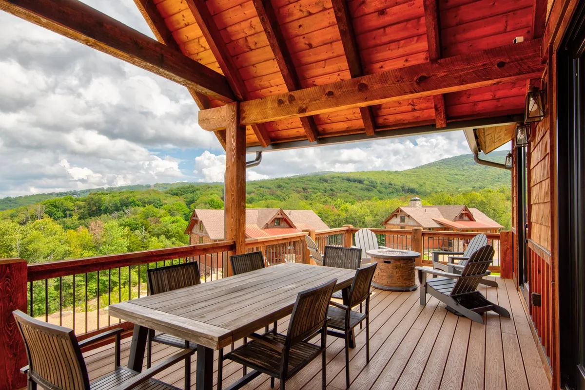 A spacious wooden deck furnished with a large dining table and black wooden chairs, offering direct views of the scenic mountains. The rustic wooden beams overhead provide a touch of shelter, while comfortable lounge chairs invite guests to relax and take in the fresh mountain air.