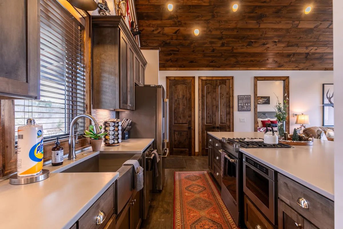 This image showcases a welcoming kitchen with a central island, stainless steel appliances, warm wooden cabinetry, and decorative items arranged on the countertop. There's a cozy rug underfoot, inviting guests to gather around the island for casual conversation or meal prep. The space feels designed for both function and sociability, echoing the section’s emphasis on creativity and togetherness in the kitchen.
