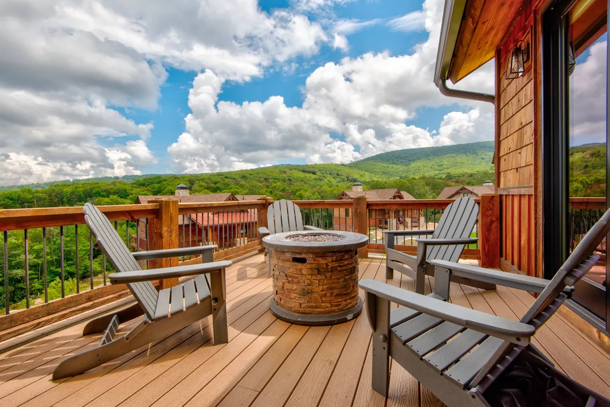A cozy fire pit area bordered by Adirondack chairs, overlooking scenic mountain vistas. The circle of chairs encourages conversation and marshmallow roasting under the stars, embodying the campfire experience.