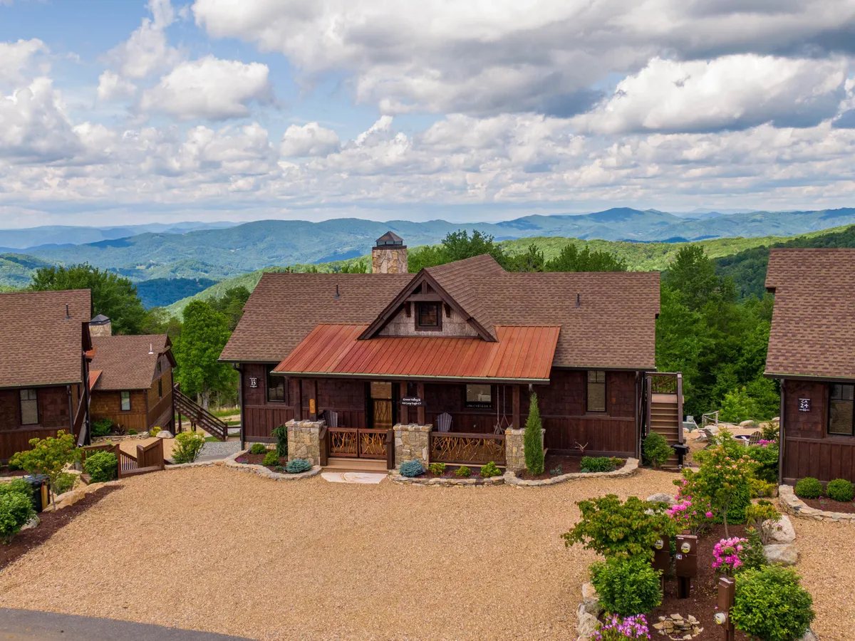 The main house is nestled against a majestic mountain backdrop with a beautifully landscaped garden and a gently curving stone pathway. The wide open outdoor space suggests ample room for walks, play, and exploration.