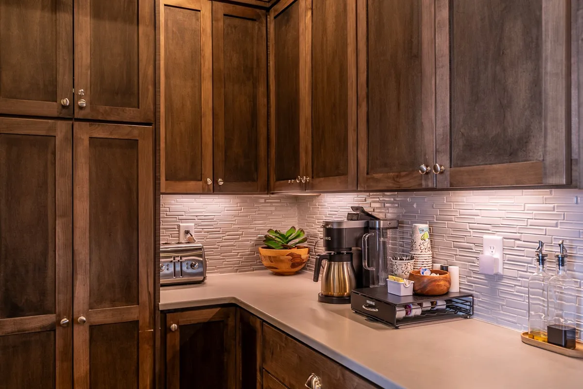 A close view of kitchen amenities, featuring dark wood cabinetry, modern countertop appliances (including a coffee maker similar to the K-Duo Plus), and a textured backsplash. A touch of greenery in a wooden bowl adds warmth and freshness, while the setup encourages morning coffee rituals and culinary adventure.