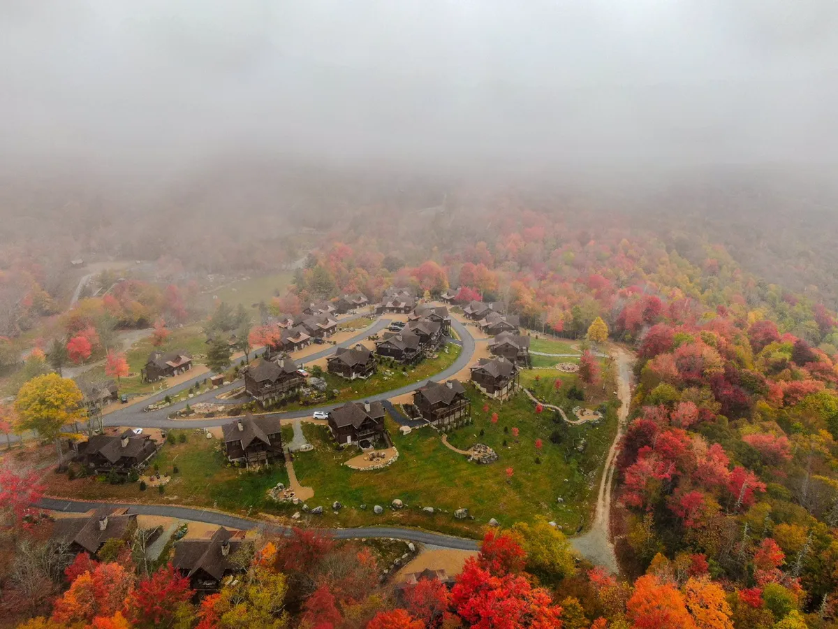 A stunning exterior shot showcasing vibrant autumn foliage along a curved road with a cluster of homes nestled in the mountains. The colors evoke the beauty of fall, encouraging exploration and romantic walks amidst nature’s seasonal splendor.