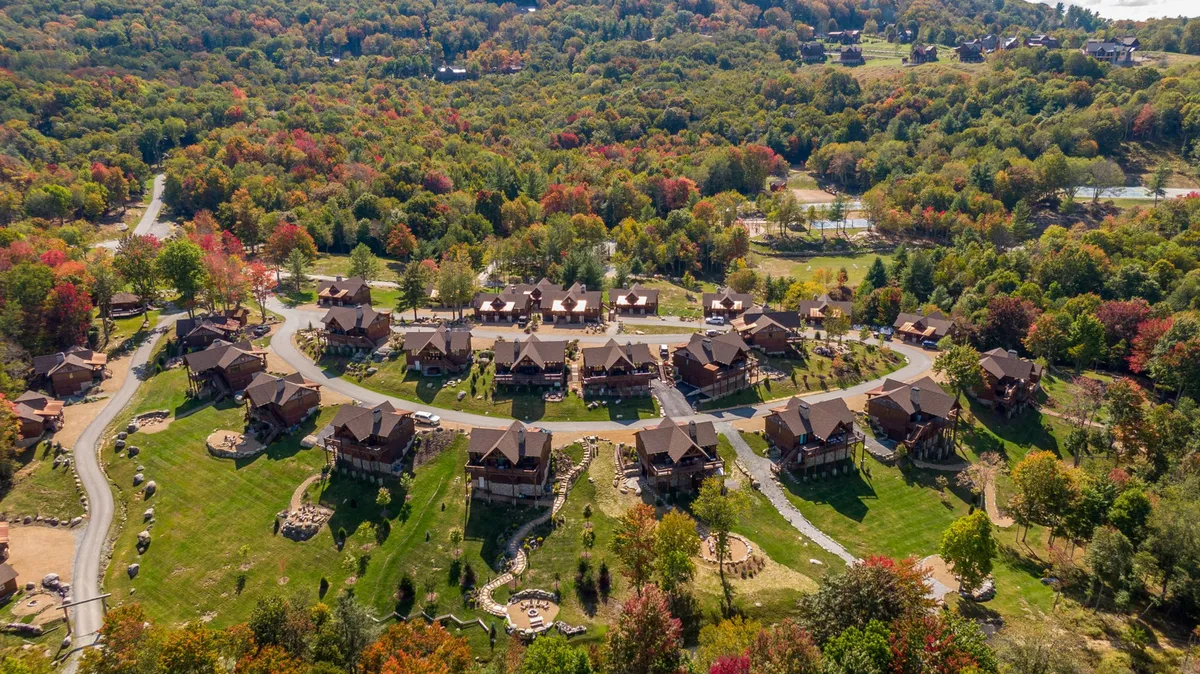 A cluster of charming cabins nestled among trees and a winding road, with mountains rising in the distance. The scene conveys a sense of community nestled in nature, inviting exploration and outdoor adventures.