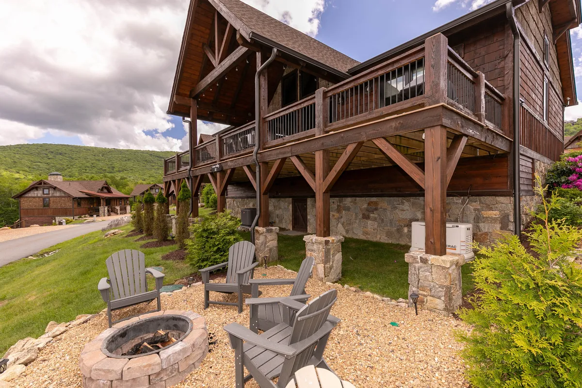 A large, inviting wooden house with stone columns, a cozy fire pit surrounded by Adirondack chairs, and open views of the mountains. The setting is ideal for enjoying evenings outdoors, socializing, and basking in the natural beauty that surrounds the community.